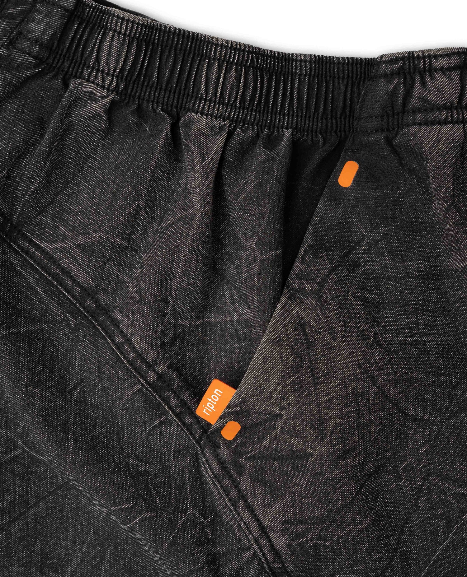 Close-up of black pants with orange accents and a brand logo on a white background