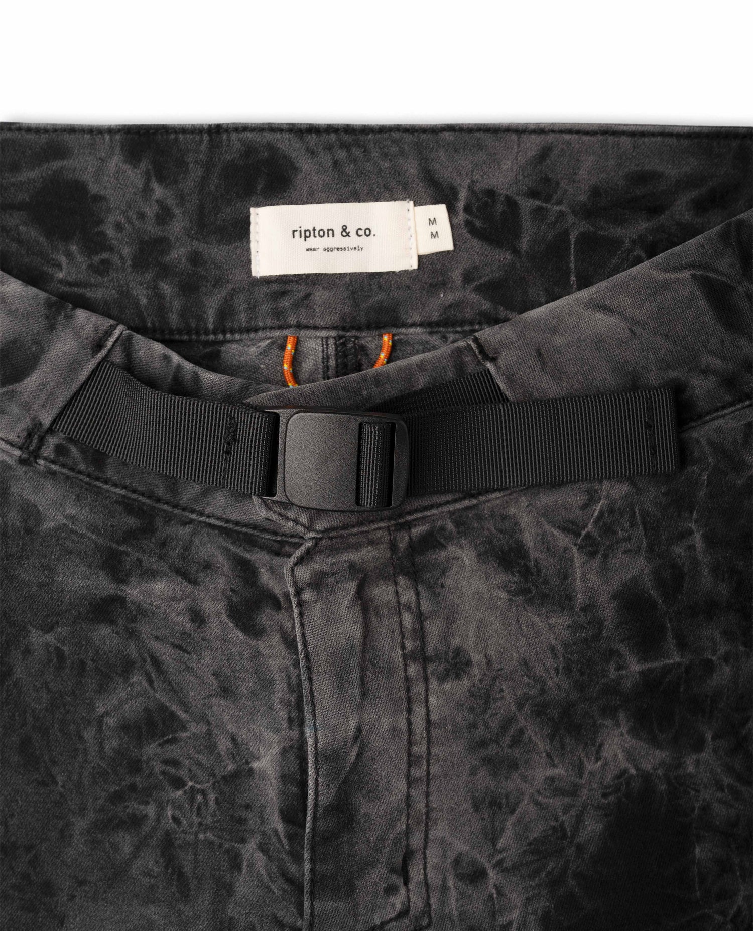 Close-up of a black belt with a buckle on a patterned fabric background, featuring the brand 'ripton & co'.