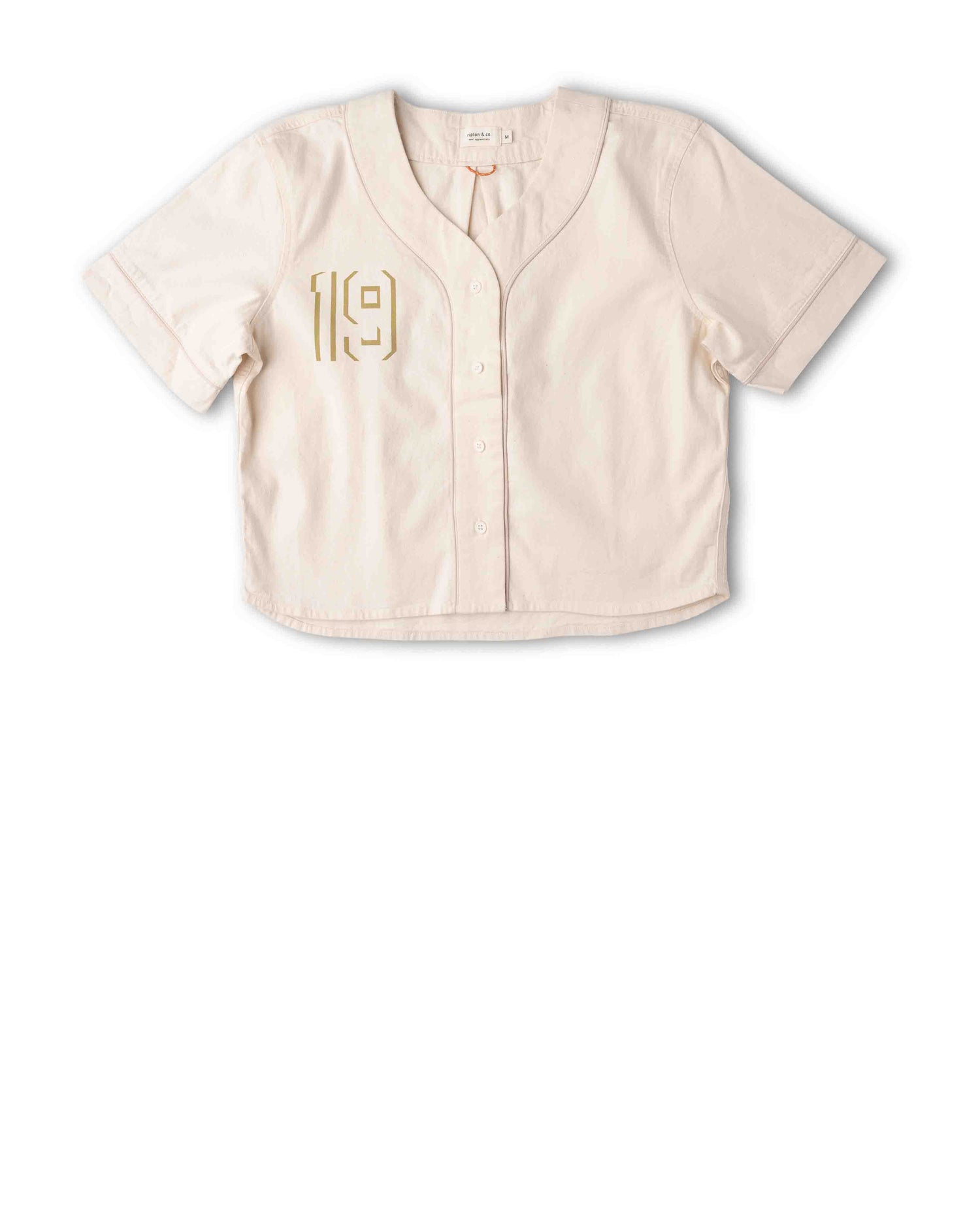 A short-sleeve button-front crop top in a light cream or off-white color, featuring a gold vertical stripe detail on the left chest and a V-neckline, laid flat against a white background.