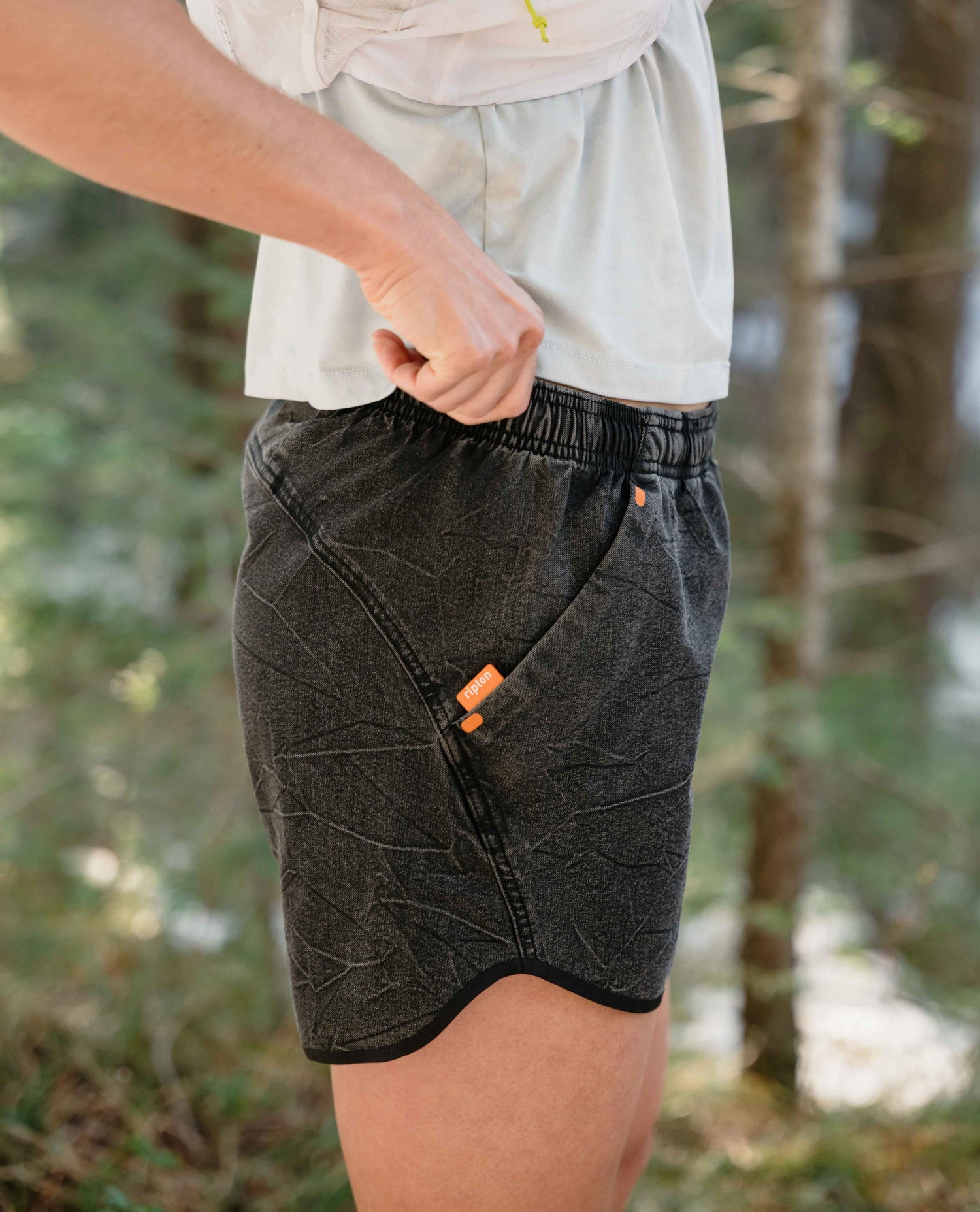 Person wearing black shorts with orange details in a forest setting