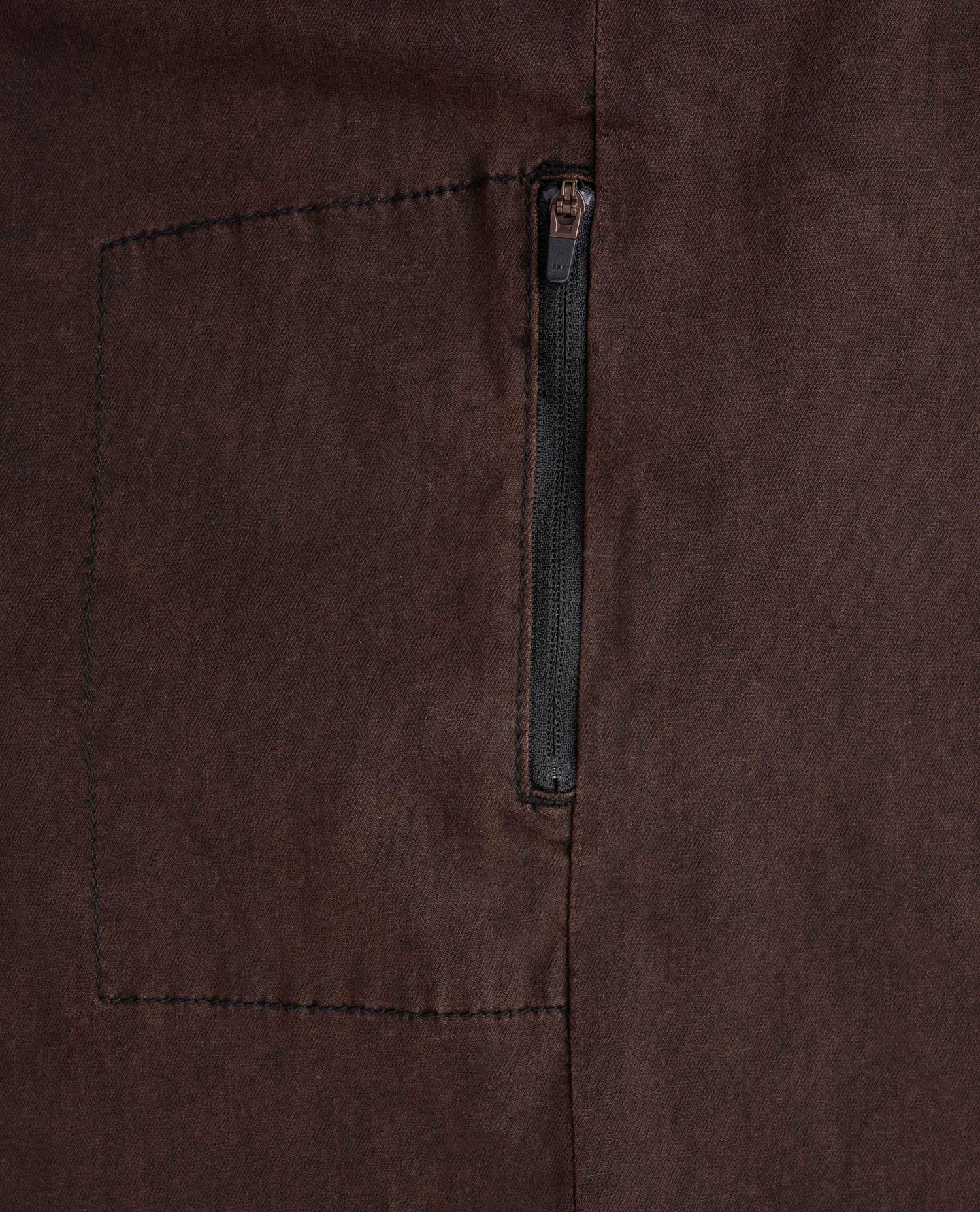 Close-up of a brown fabric pocket with a zipper on a matching brown background