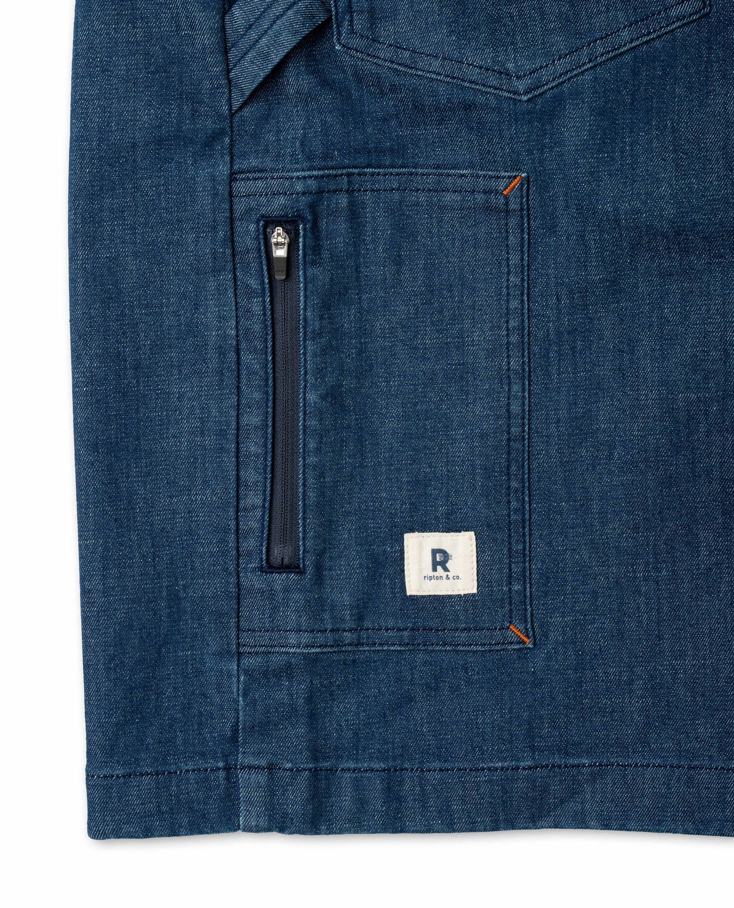Close-up of a blue denim shirt with a zipper pocket and brand logo on a white background