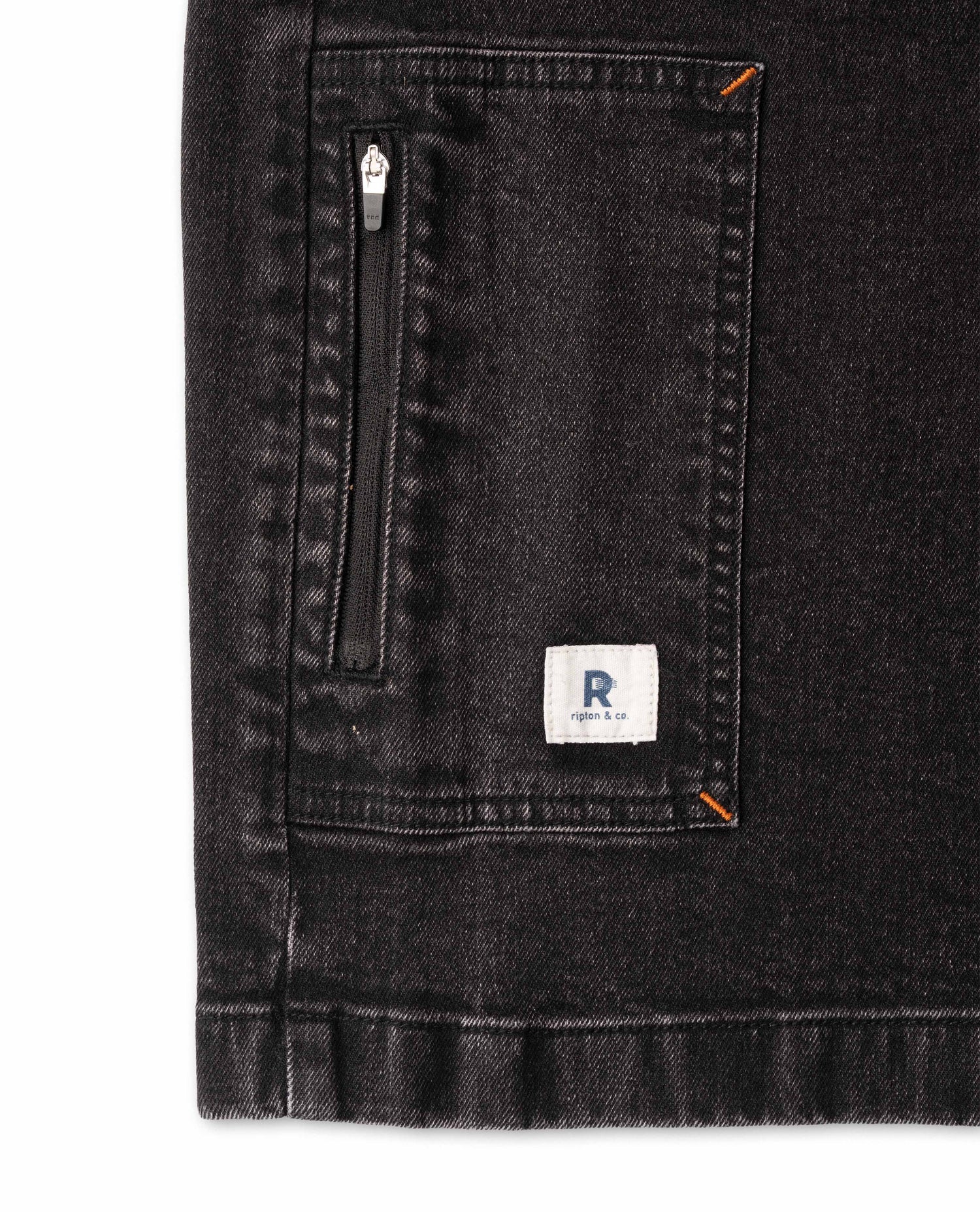 Close-up of a black denim jacket with a zipper pocket and a brand logo on a white background