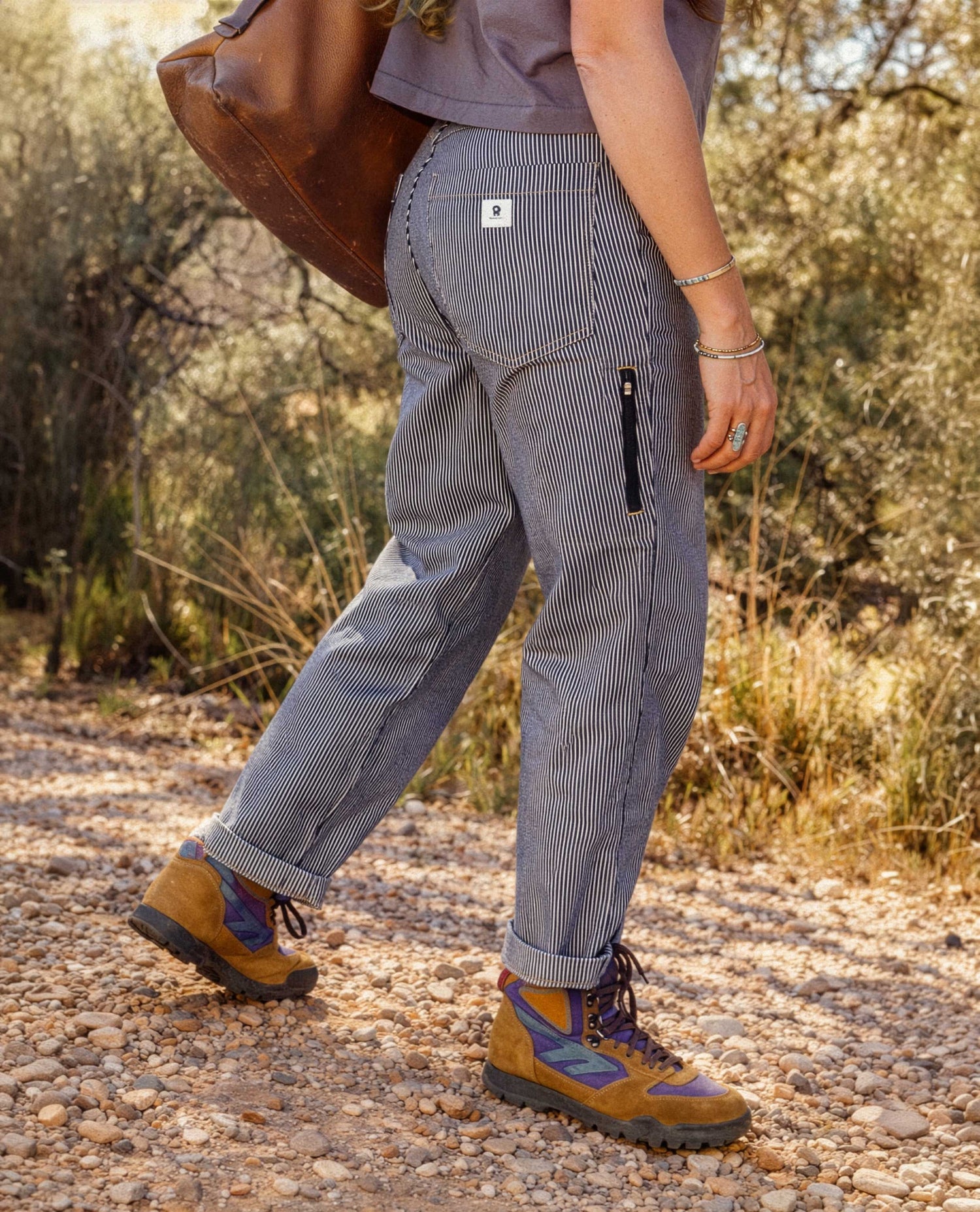 Person wearing gray checkered pants with a visible brand logo, walking on a dirt path in a natural setting.