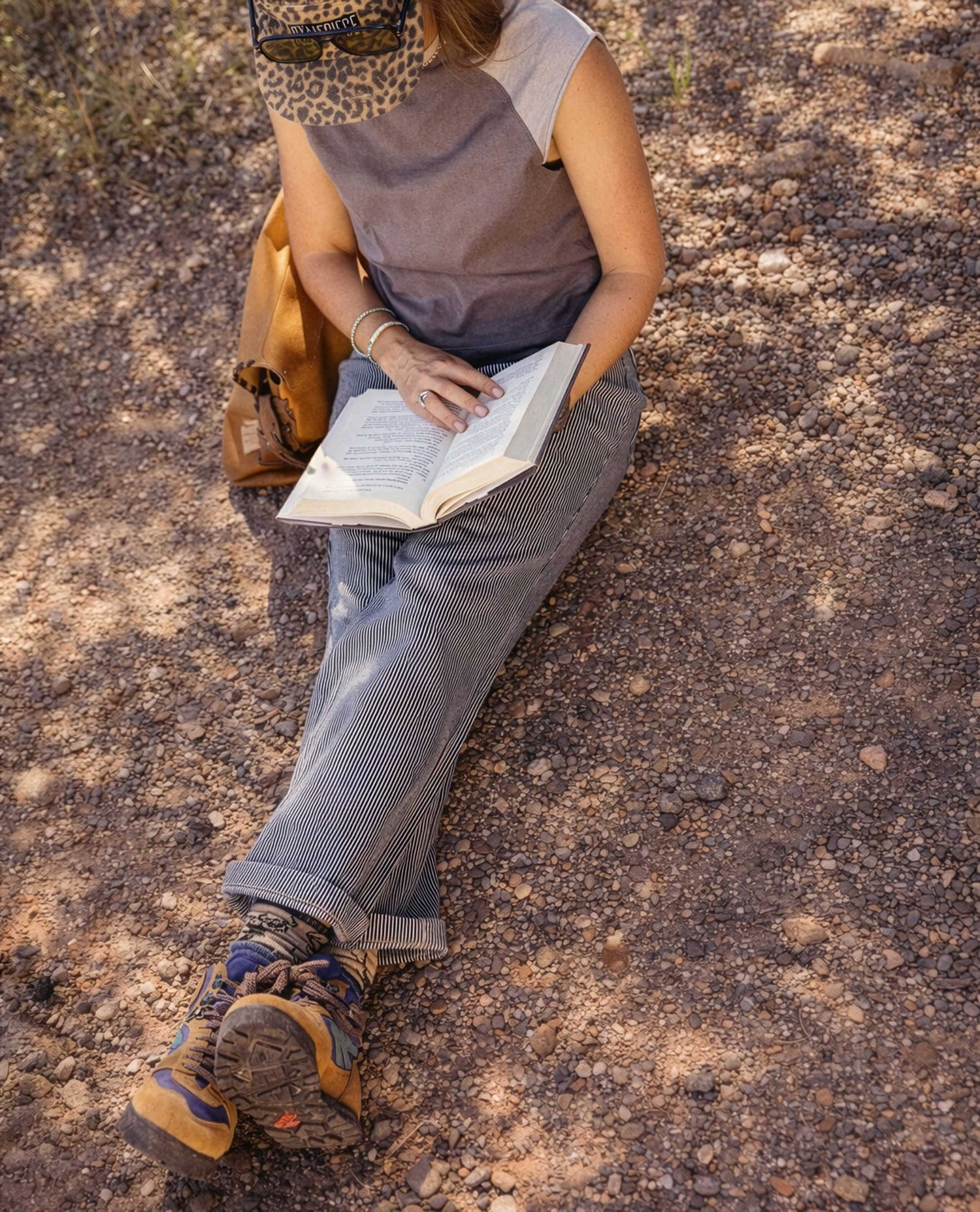 Person sitting on a rocky surface reading a book with a backpack next to them.
