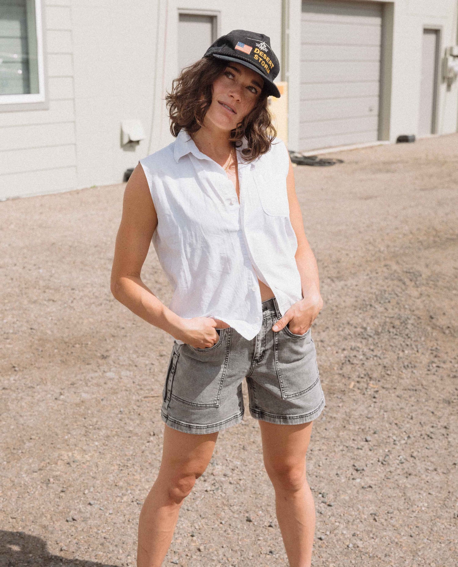 Person wearing a white sleeveless shirt and denim shorts standing outdoors.