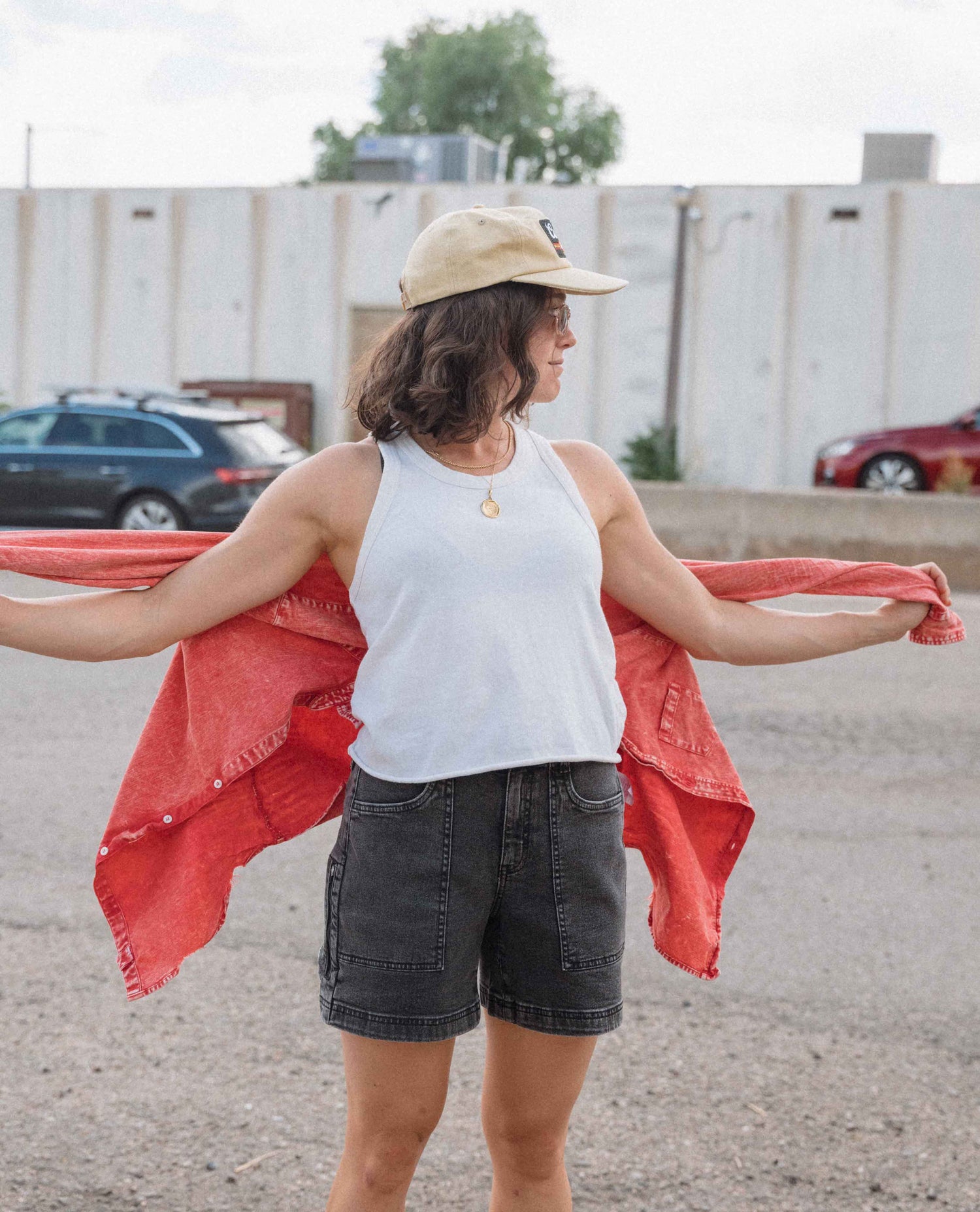 Woman wearing a white tank top and denim shorts with a red shawl, standing outdoors.
