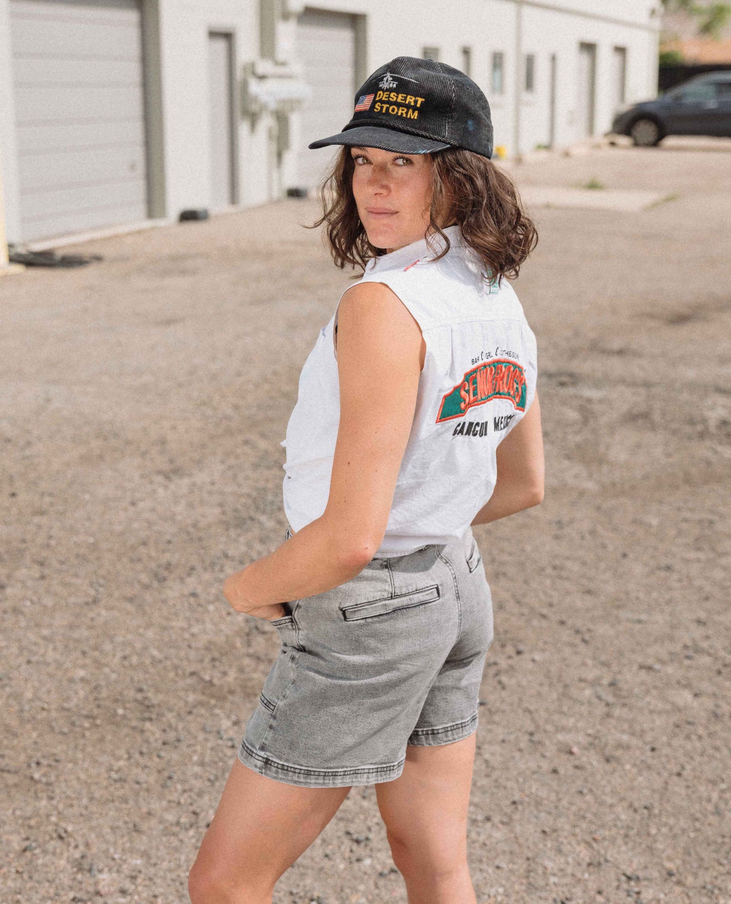 Person wearing a sleeveless shirt with a logo and a cap in an outdoor setting.