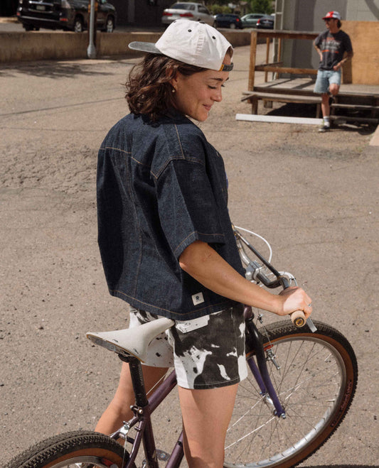 Person wearing a denim shirt and white cap with a bicycle, standing on a concrete surface.