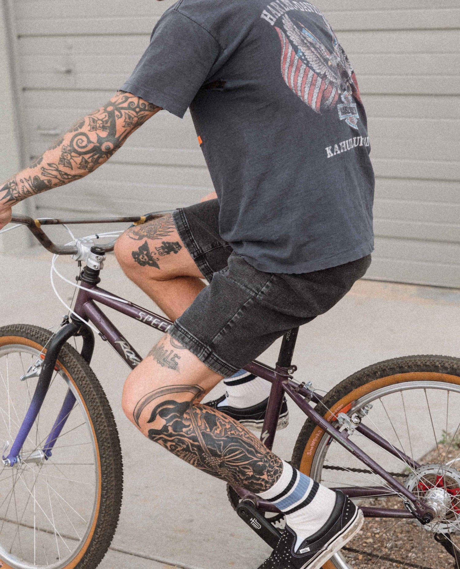 Person riding a bicycle wearing a dark t-shirt with visible tattoos.
