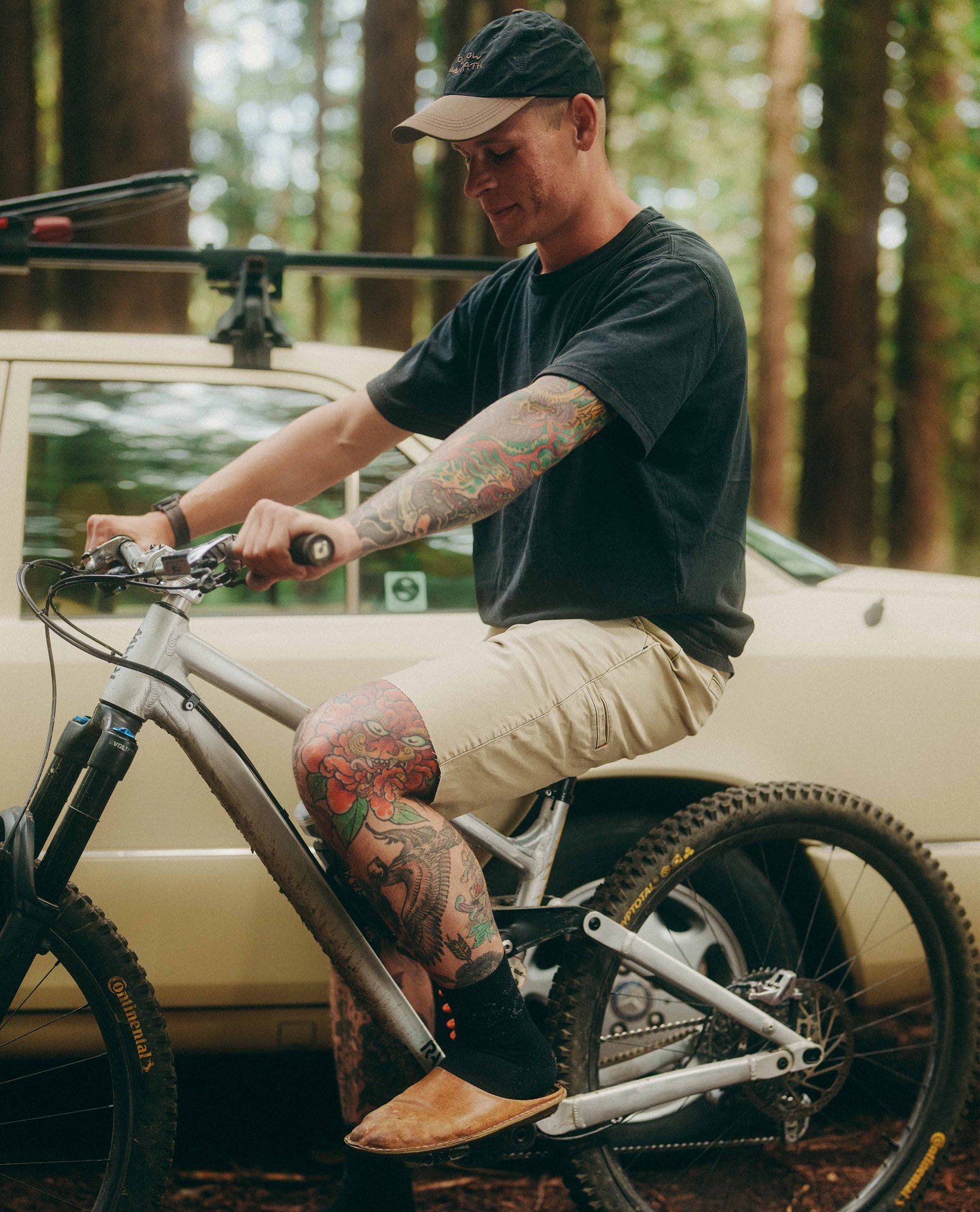 Man with tattoos sitting on a bicycle in a forested area