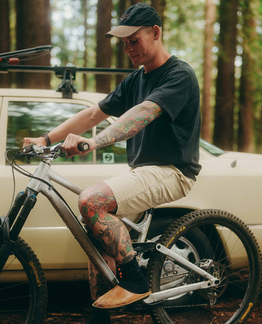 Man with tattoos sitting on a bicycle in a forested area
