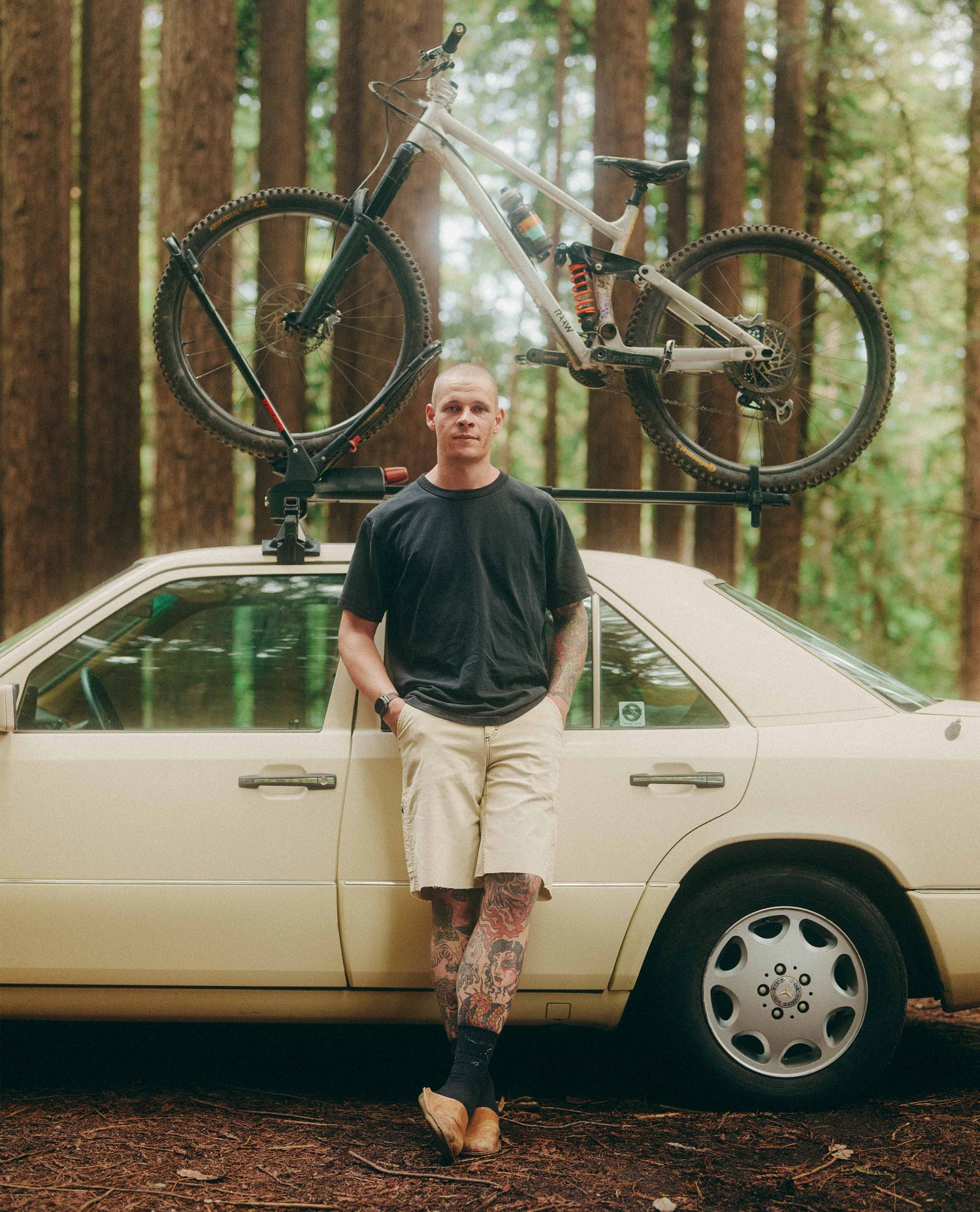 Man standing next to a car with a bicycle on a rack in a forest.
