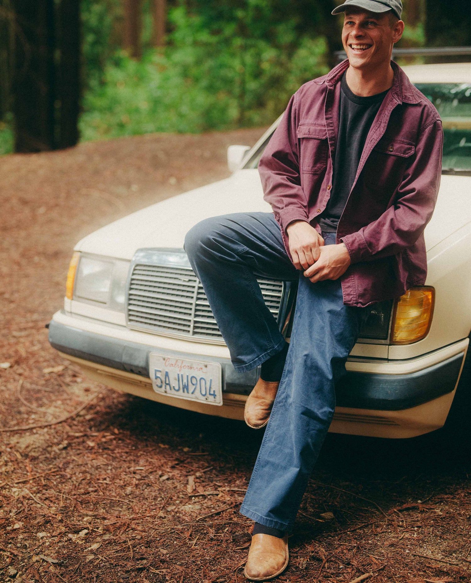 Man sitting on a white car in a forested area
