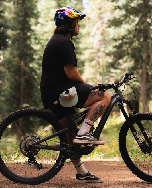 Man sitting on bike with blue helmet, black clothes, outside in the woods 
