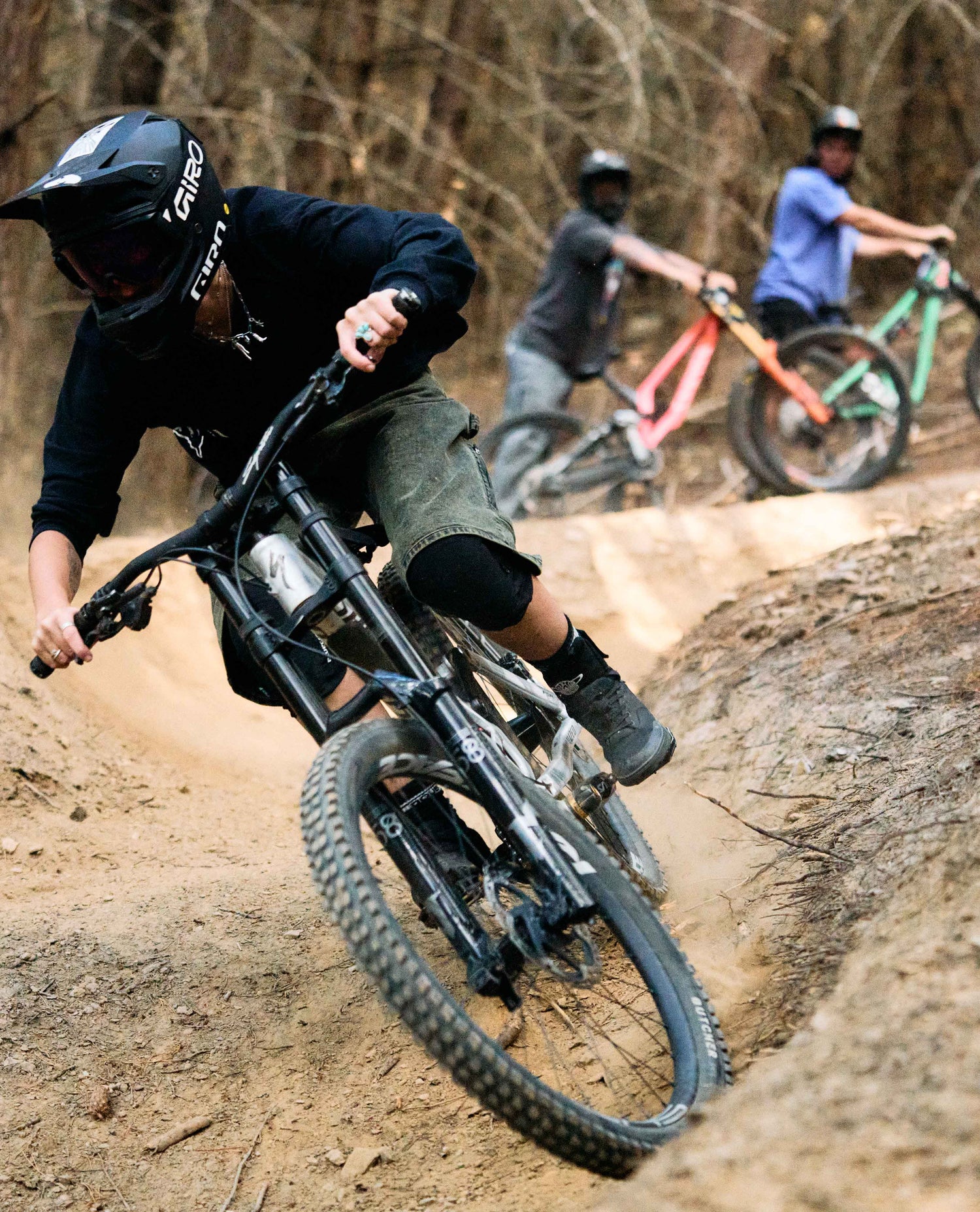 Person riding a mountain bike on a dirt trail with two other riders in the background.