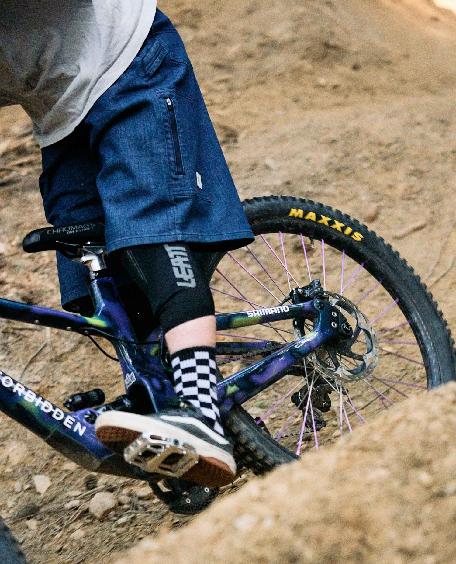 Person riding a mountain bike on a dirt trail with 'Leatt' and 'Maxxis' branding visible.