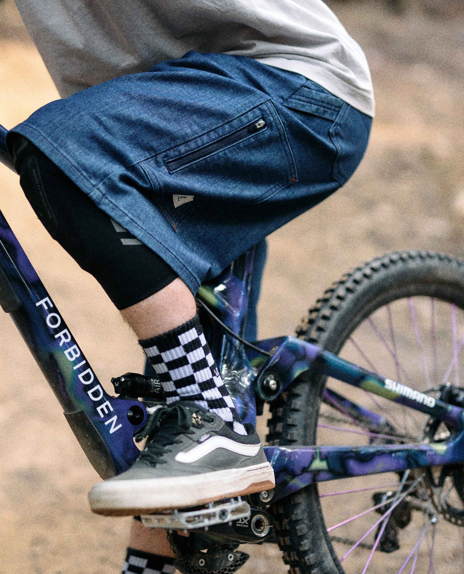 Person riding a bicycle wearing blue shorts and checkered socks.