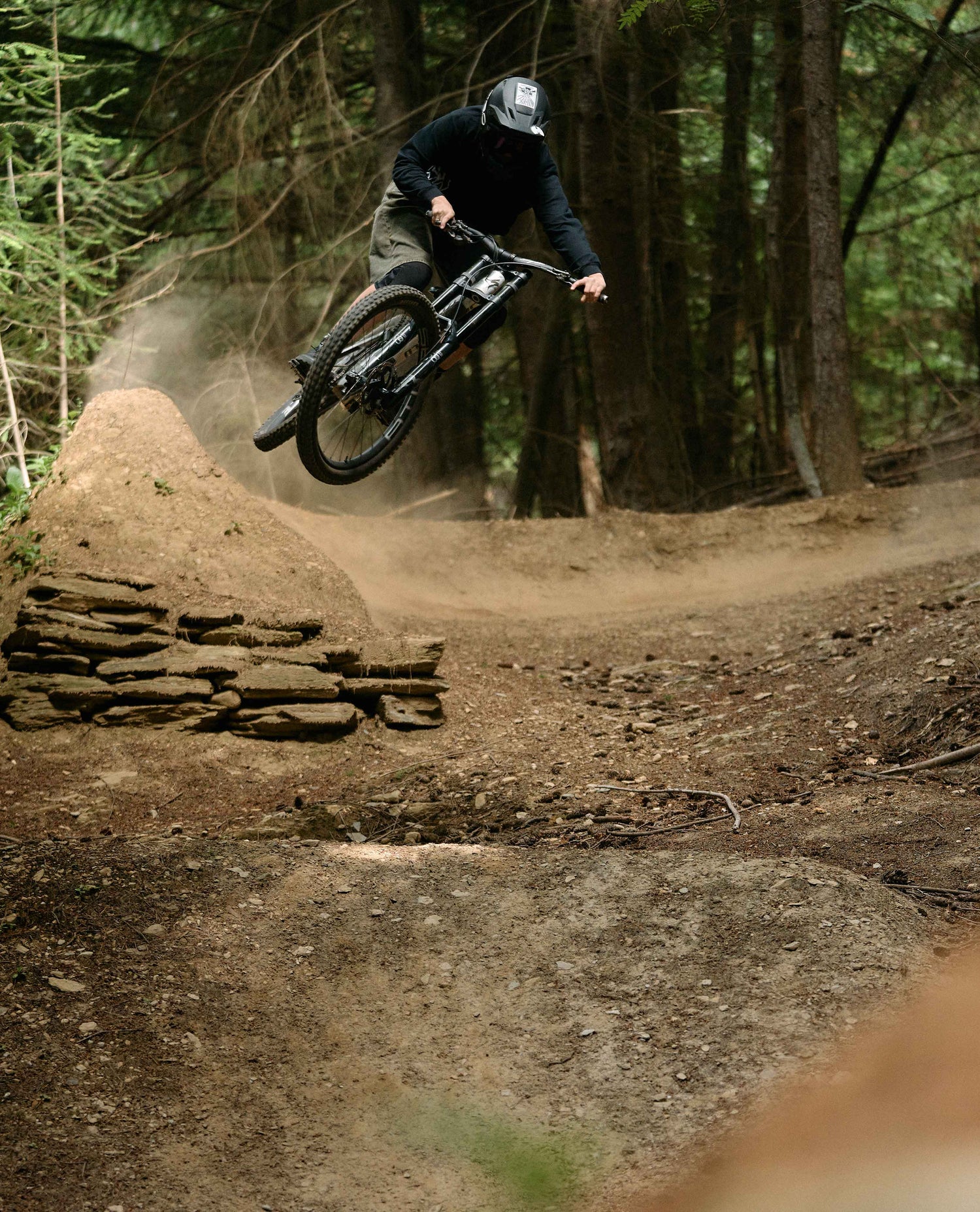 Person riding a mountain bike on a dirt trail with trees in the background