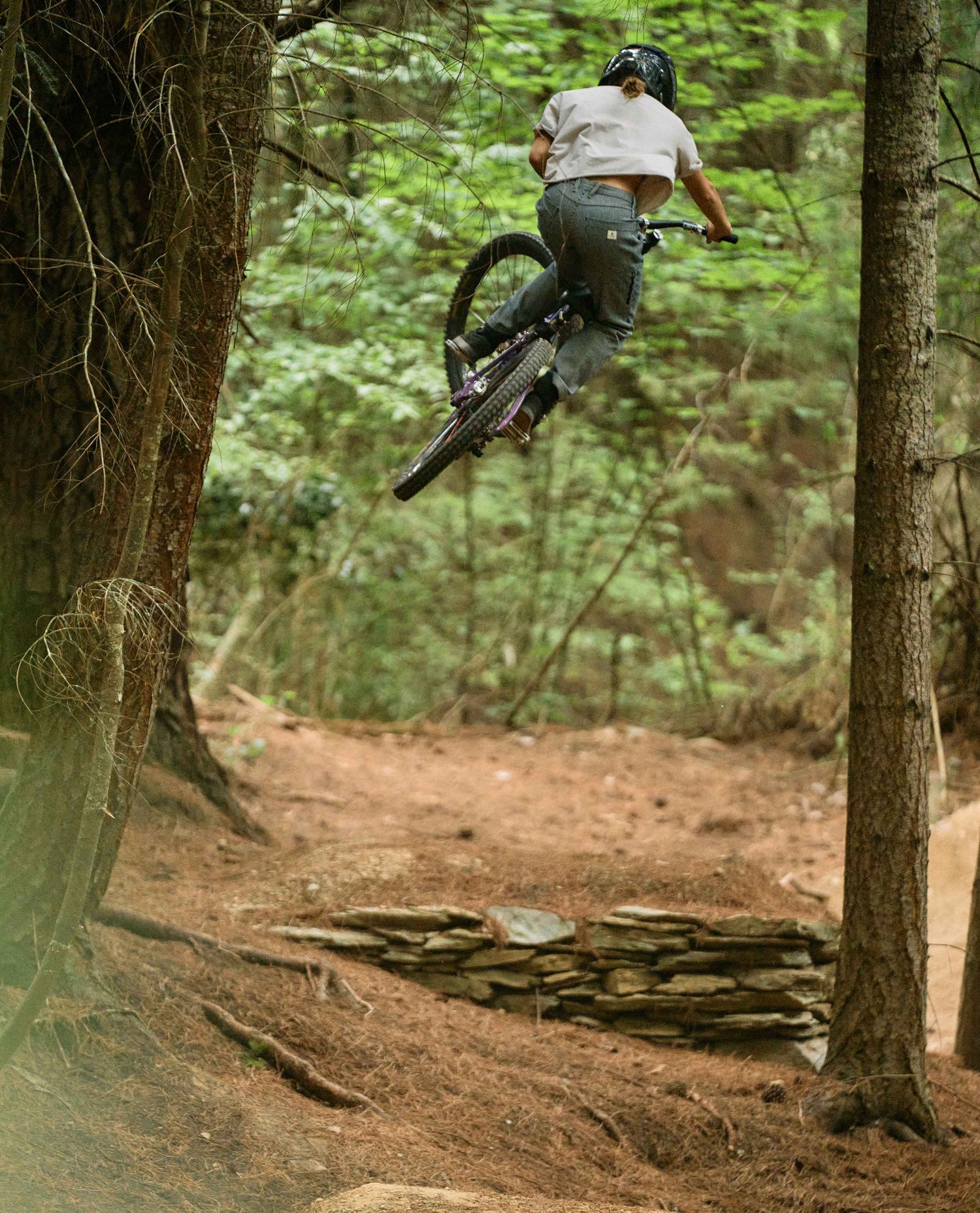 Person on a mountain bike in mid-air over a dirt jump in a forest