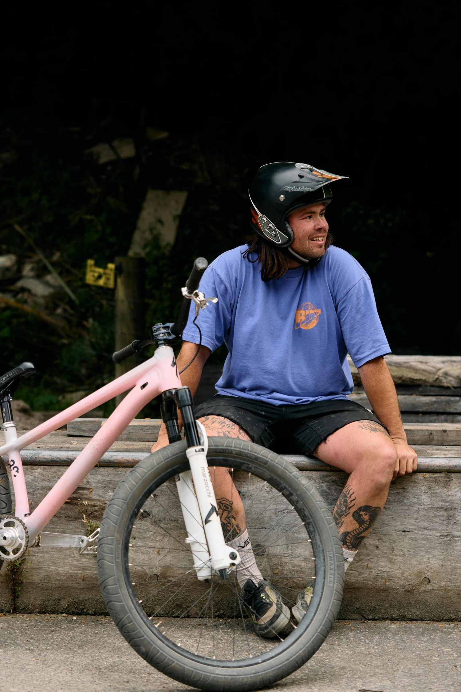 Man sitting on a wooden ledge with a bicycle, wearing a helmet and blue shirt.