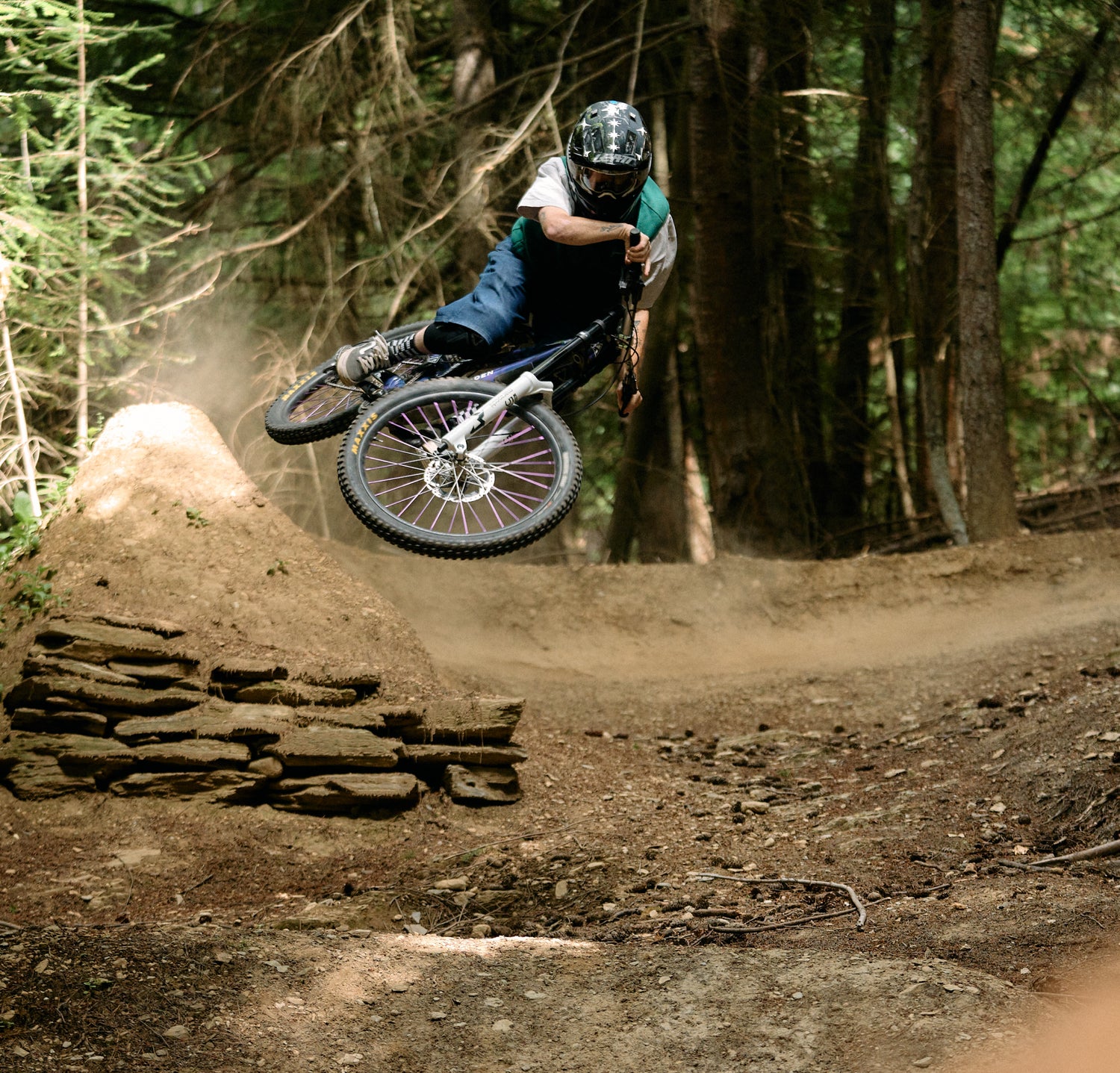 Person on a bike in mid-air over a dirt jump with trees in the background