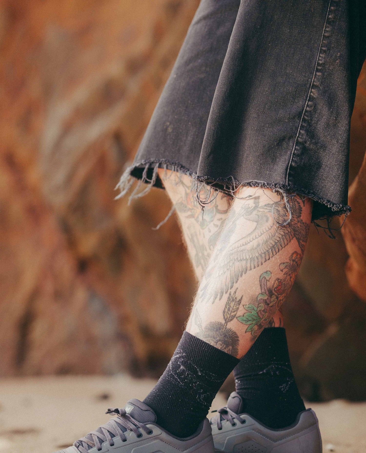 Tattooed legs wearing black socks and gray sneakers with a blurred natural background