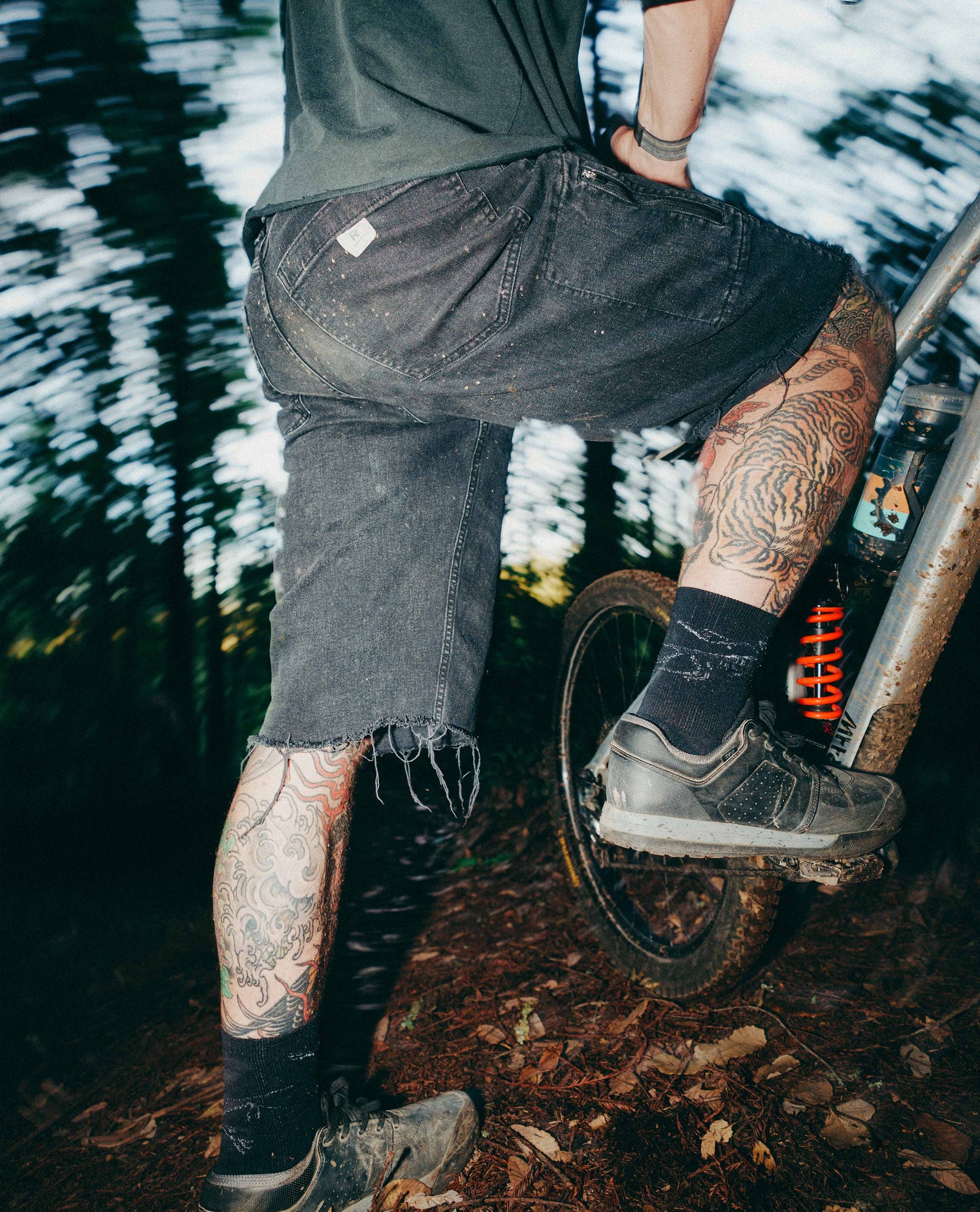 Person with tattoos riding a unicycle in a forest setting