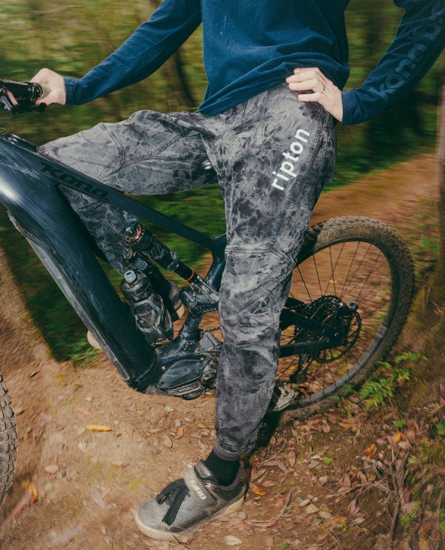 Person wearing gray pants with 'Ripton' branding on a bike in a forest setting
