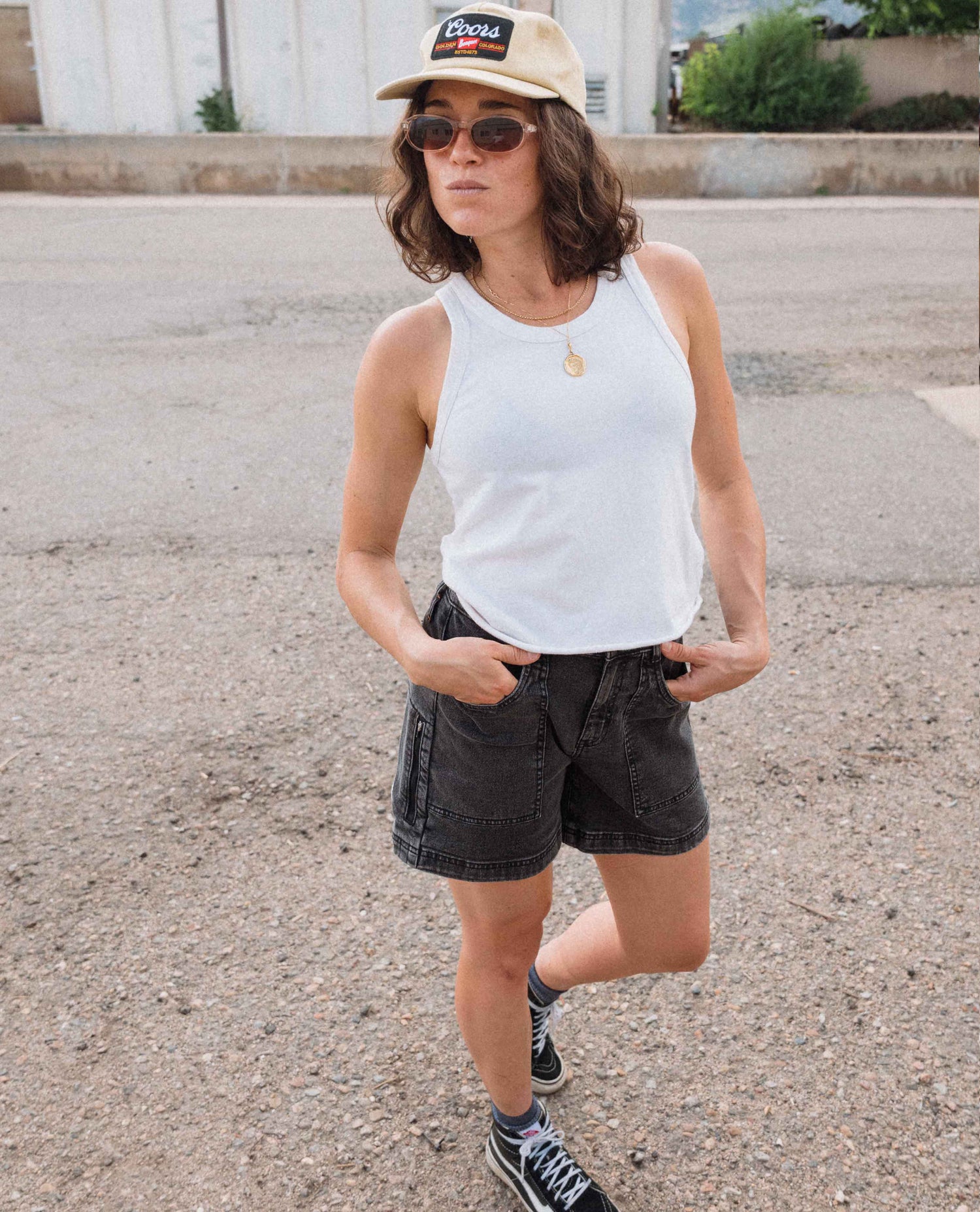 Person wearing a white tank top, black shorts, and a beige cap outdoors.