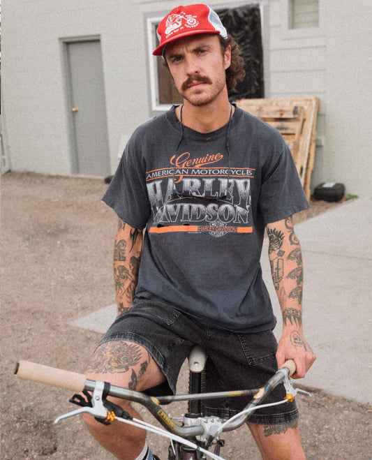 Man wearing a Harley Davidson t-shirt and red cap sitting on a bicycle.