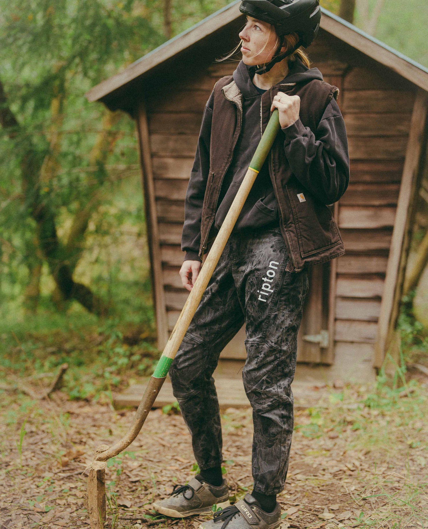Person in outdoor setting holding a long tool, wearing a helmet and dark jacket.